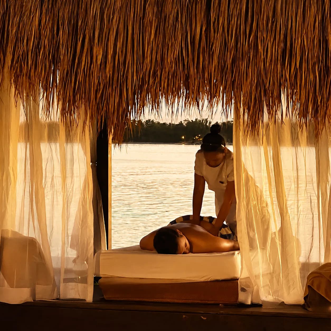 A guest receiving a massage in a waterside tropical spa pavilion
